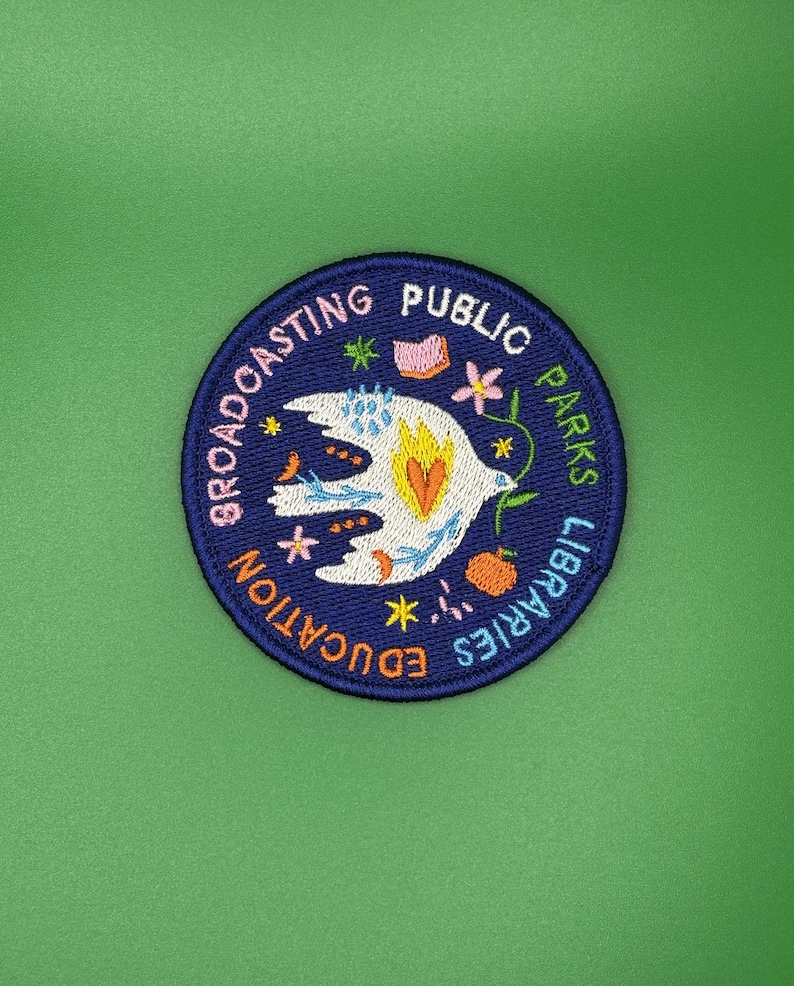 Pode incluir: Patch bordado com borda azul marinho e fundo verde. O patch apresenta as palavras "Broadcasting Public Parks Libraries Education" em um padr&atilde;o circular. Um p&aacute;ssaro branco com detalhes em laranja e amarelo est&aacute; no centro.