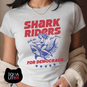 Shark Riders for Democracy Baby Tee | Ride the Blue Wave | Girl Riding Shark Design, Shark T-Shirt, Stormy T-shirt, Shark T-shirt