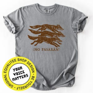 May include: A gray t-shirt featuring a brown illustration of three running foxes. The text "&iexcl;NO PASAR&Aacute;N!" is printed below the foxes. The shirt has a crew neck and short sleeves.