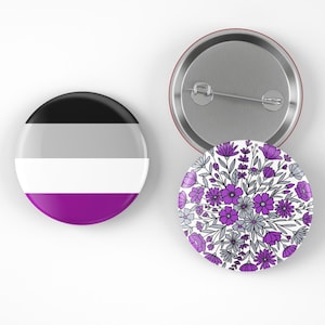 May include: Three round buttons. One button features the asexual pride flag with black, gray, white, and purple stripes. Another button has a floral design in purple and gray on a white background. The third button is a silver pin back.
