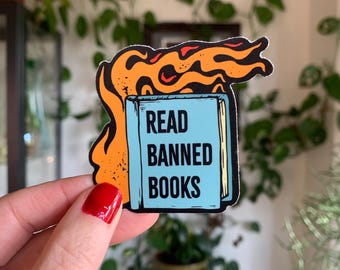 May include: A blue book with the text "READ BANNED BOOKS" on the cover is engulfed in orange flames. The book is a sticker.