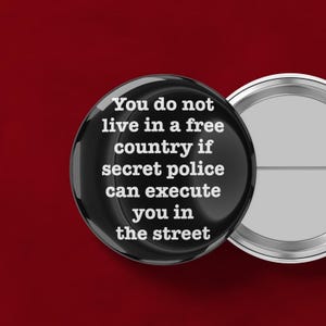 May include: A black button with the text "You do not live in a free country if secret police can execute you in the street" in white. The button is on a red background.