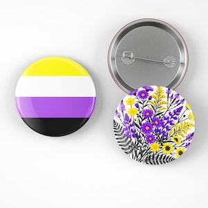 Puede incluir: Dos botones redondos. Un botón presenta la bandera del orgullo no binario con rayas amarillas, blancas, moradas y negras. El otro botón tiene un diseño floral con flores moradas y amarillas.