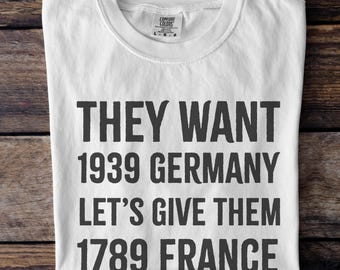 May include: White t-shirt with black text that reads "They want 1939 Germany Let's give them 1789 France".