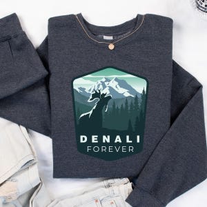 May include: Dark gray sweatshirt with a green, blue, and white mountain scene with a moose silhouette. The text "DENALI FOREVER" is printed below the scene.