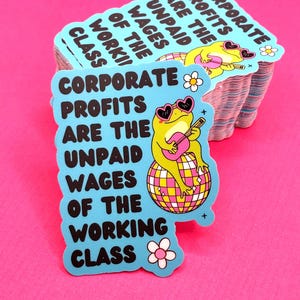 May include: A stack of light blue stickers with the text "CORPORATE PROFITS ARE THE UNPAID WAGES OF THE WORKING CLASS". Each sticker features a cartoon frog wearing heart-shaped sunglasses and playing a guitar on a disco ball.
