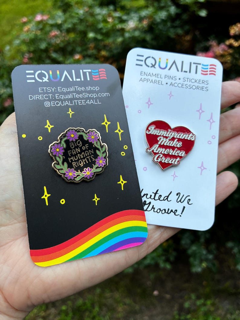 Pu&ograve; includere: Due spille smaltate su cartoncini. Una spilla recita "Big Fan of Human Rights" circondata da fiori. L'altra spilla &egrave; a forma di cuore e recita "Immigrants Make America Great". I cartoncini hanno disegni arcobaleno e stelle.