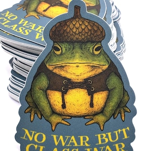 May include: A stack of stickers featuring a detailed illustration of a frog wearing an acorn hat and vest. The frog has green skin and a yellow belly. The text "NO WAR BUT CLASS WAR" is printed in yellow on a blue background.