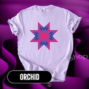May include: A light purple t-shirt featuring a geometric star design in shades of pink and blue. The word "ORCHID" is displayed in a black rectangle at the bottom. The shirt is a comfortable, casual style.