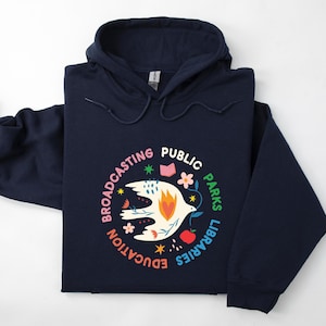 May include: Navy blue hooded sweatshirt with a colorful circular graphic. The graphic features a white bird with a heart, surrounded by the words "Broadcasting Public Parks Libraries Education". The design includes flowers, a book, and an apple.