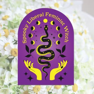 May include: A purple sticker with the text "Spooky Liberal Feminist Witch" in yellow. The sticker features a black snake with yellow stars, surrounded by moon phases and held by yellow hands.