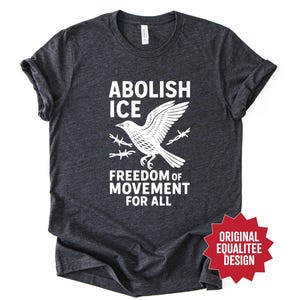 May include: Dark gray t-shirt with white text and graphic. The text reads "ABOLISH ICE" above a bird graphic with barbed wire, and "FREEDOM OF MOVEMENT FOR ALL" below. A red starburst graphic says "ORIGINAL EQUALITEE DESIGN".