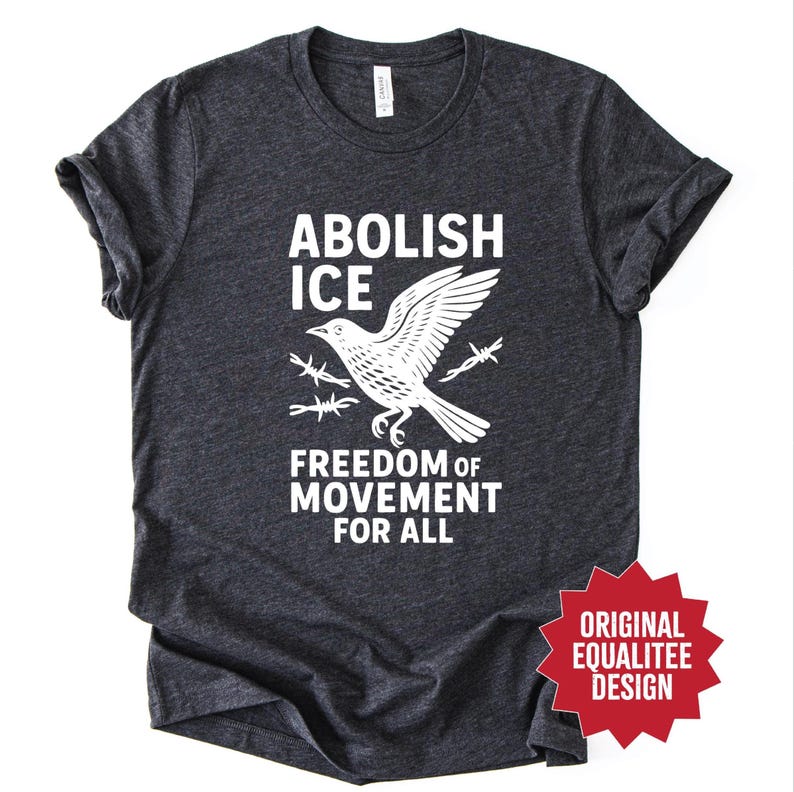 May include: Dark gray t-shirt with white text and graphic. The text reads "ABOLISH ICE" above a bird graphic with barbed wire, and "FREEDOM OF MOVEMENT FOR ALL" below. A red starburst graphic says "ORIGINAL EQUALITEE DESIGN".
