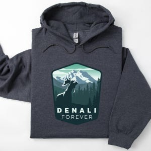 May include: A dark gray hooded sweatshirt with a graphic design of a mountain range and a deer silhouette. The text "DENALI FOREVER" is printed below the graphic.
