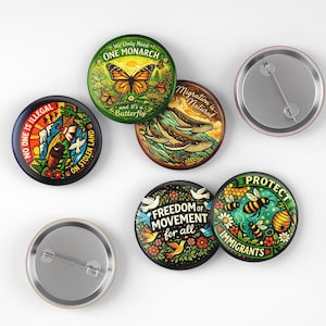 May include: A collection of round button pins with various designs and text. One pin features a monarch butterfly, another says "No One Is Illegal", and others display phrases like "Freedom of Movement" and "Protect Immigrants". The pins have a metal backing.