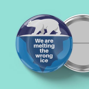 May include: A round button with a white polar bear on a blue and white iceberg design. The text "We are melting the wrong ice" is printed on the button. The button has a metal backing.