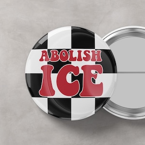 May include: A round button with a black and white checkered background. The button features the words "ABOLISH ICE" in red, bold letters. A second button is partially visible in the background.