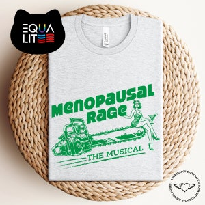 May include: A gray t-shirt with a green graphic of a woman riding a chainsaw with the text "Menopausal Rage The Musical".