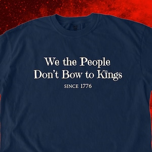 K&ouml;nnte beinhalten: Marineblaues T-Shirt mit dem wei&szlig;en Text "We the People Don't Bow to Kings SINCE 1776". Das T-Shirt hat einen Rundhalsausschnitt und kurze &Auml;rmel. Der Text ist mittig auf der Vorderseite des Shirts platziert.