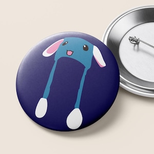 May include: A round button with a cartoon illustration of a blue hat with long dangling legs and white feet. The hat has pink inner ears and a smiling face. The button is set against a dark blue background.