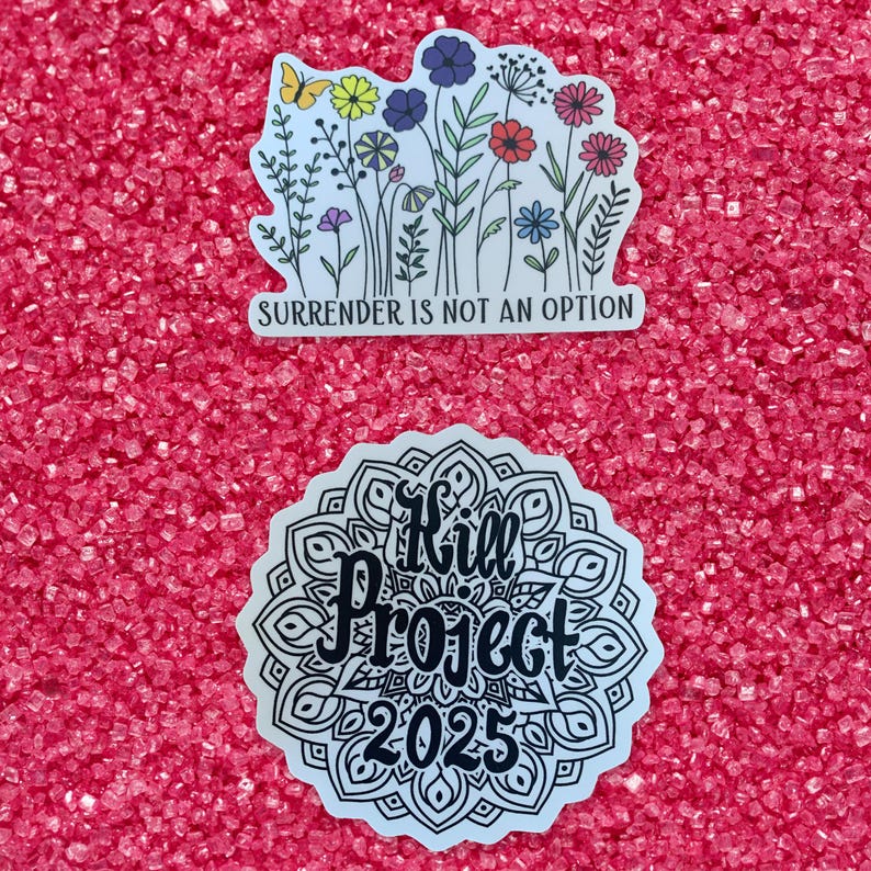 May include: Two stickers on a pink background. The top sticker features a floral design with the text "Surrender is not an option". The bottom sticker features a black and white mandala design with the text "Kill Project 2025".