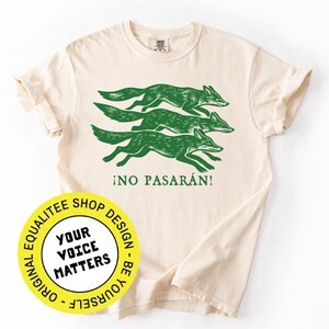 May include: Cream-colored t-shirt featuring a green graphic of three running foxes and the Spanish phrase "&iexcl;NO PASAR&Aacute;N!". A yellow circular logo with the text "YOUR VOICE MATTERS" is also visible.
