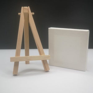 Könnte beinhalten: Ein kleiner Holzstaffelei mit einer weißen Leinwand.