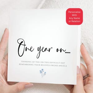 May include: A white square card with black script reading "One year on..." and the message "Thinking of you on this difficult day remembering your beloved friend Angela." A red square in the corner says "Personalise With Any Name or Relation."