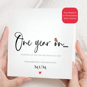 Peut inclure: Une carte de vœux carrée blanche avec le texte noir One year on et une petite illustration d'un rouge-gorge. En dessous, le texte indique Thinking of you on this difficult day, Remembering your beloved Mum, et une petite icône de cœur rouge.