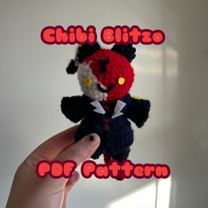 May include: A crocheted doll with a red and white face, black ears, and a navy blue suit. The doll has yellow eyes and a smiling expression. The image includes the text "Chibi Blitzo" and "PDF Pattern".