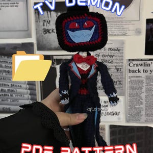 Könnte beinhalten: Gehäkelte TV-Dämon-Puppe mit schwarzem Fernseh-Kopf, roten Augen und einer blauen Maske. Die Puppe trägt einen dunkelblauen Anzug mit roten Akzenten und eine rote Fliege. Der Text "TV DEMON" und "PDF PATTERN" ist sichtbar.