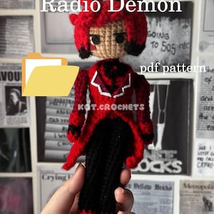 May include: A handmade crochet doll of the Radio Demon character, featuring a red and black color scheme. The doll has a detailed design, including a red coat, black pants, and a distinctive headpiece. The text "Radio Demon" and "pdf pattern" are visible.