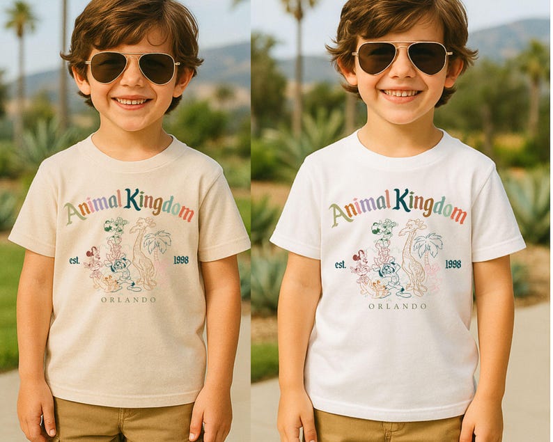 K&ouml;nnte beinhalten: Zwei kurz&auml;rmelige T-Shirts, eines cremefarbenes und eines wei&szlig;es, zeigen den Text "Animal Kingdom" in Regenbogenfarben, mit einer Grafik von Zeichentieren und dem Text "Orlando 1998".