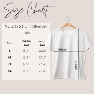 Op de afbeelding: Een wit T-shirt met korte mouwen voor jongeren, hangend aan een houten hanger. De afbeelding bevat een maattabel met afmetingen in centimeters voor breedte en lengte. De tabel vermeldt de maten S, M, LT en XL.