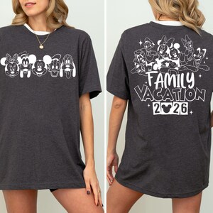 Peut inclure: T-shirt gris fonc&eacute; avec bordure blanche. Le devant pr&eacute;sente des visages de personnages Disney, tandis que le dos affiche un groupe de personnages et le texte "FAMILY VACATION 2026".