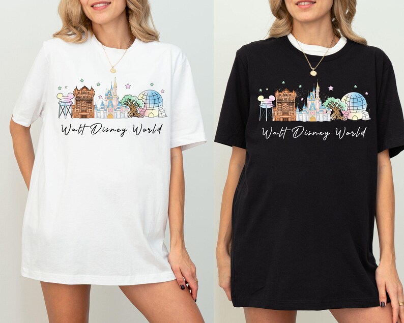 May include: A white t-shirt and a black t-shirt, each featuring a graphic print of the Walt Disney World skyline. The design includes iconic park landmarks in pastel colors, small stars, and the text Walt Disney World in a black cursive script.