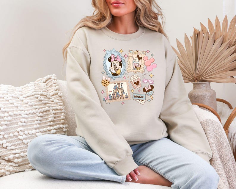Pu&ograve; includere: Felpa beige con un colorato collage di immagini di cartoni animati. Il design include Minnie Mouse, popcorn, un castello e la parola "MAGIC". La felpa ha maniche lunghe e girocollo.