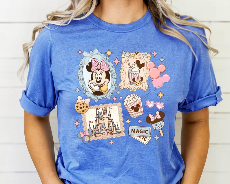 Pu&ograve; includere: T-shirt blu con una grafica colorata raffigurante Minnie Mouse, un castello, popcorn e gelato. Il design include la parola "MAGIC" e altri elementi a tema, il tutto incorniciato da stelle e bordi decorativi.