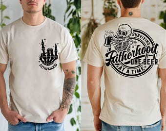 Può includere: T-shirt beige con grafica nera. Davanti, una mano di scheletro che fa il gesto rock and roll, con la parola «FATHERHOOD». Sul retro, uno scheletro che beve birra con la scritta «SURVIVING FATHERHOOD ONE BEER AT A TIME».