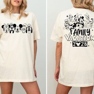 Peut inclure: T-shirt cr&egrave;me avec un motif noir et blanc de personnages Disney &agrave; l'avant. Le dos du t-shirt affiche d'autres personnages et le texte "FAMILY VACATION 2026" avec une ic&ocirc;ne de Mickey Mouse.