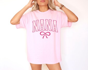 May include: A pink t-shirt with the word "NANA" printed in a pink and white collegiate font with a pink bow underneath.
