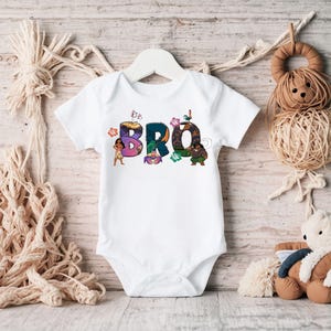 K&ouml;nnte beinhalten: Wei&szlig;er Baby-Strampler mit einem bunten Grafikdruck des Wortes "BRO" mit Figuren aus dem Animationsfilm Vaiana.