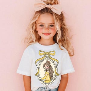 May include: A white t-shirt with a yellow and white illustration of Belle from Beauty and the Beast. The illustration is framed with a pearl necklace and a yellow bow.