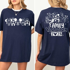 Peut inclure: T-shirt bleu marine avec bordure blanche. L'avant pr&eacute;sente une ligne de personnages de dessins anim&eacute;s, et le dos affiche "FAMILY VACATION 2026" avec d'autres personnages de dessins anim&eacute;s. Un t-shirt amusant et d&eacute;contract&eacute;.