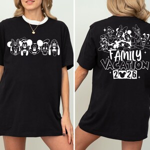 Peut inclure: T-shirt noir avec bordure blanche. Le devant pr&eacute;sente des visages de personnages de dessins anim&eacute;s. Le dos affiche des personnages de dessins anim&eacute;s, les mots "FAMILY VACATION 2026" et une t&ecirc;te de Mickey Mouse.