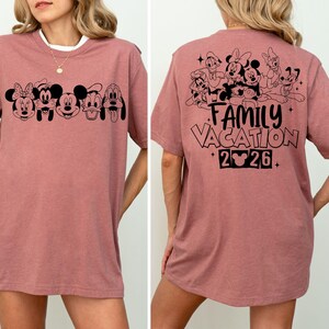 Peut inclure: T-shirt rose poudr&eacute; avec des graphiques noirs de personnages Disney. L'avant pr&eacute;sente Mickey, Minnie et leurs amis. Le dos affiche le texte "Family Vacation 2026" avec d'autres personnages. Un tee-shirt confortable et d&eacute;contract&eacute;.