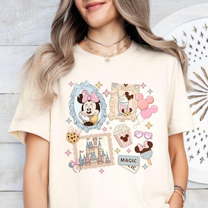 Pu&ograve; includere: T-shirt color crema con un collage a tema Disney. Il design include Minnie Mouse, un castello, popcorn, gelato e palloncini. &Egrave; presente anche la parola "MAGICAL". La maglietta ha un classico girocollo.