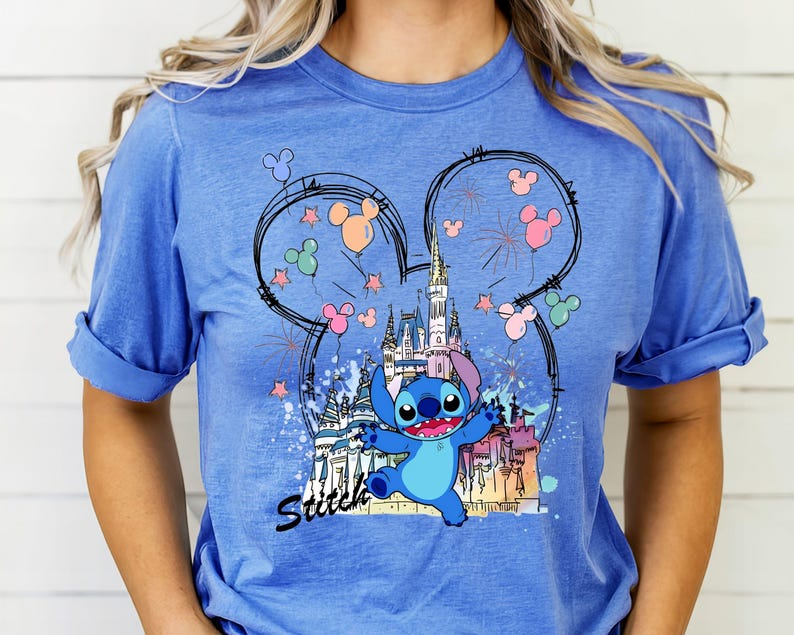 May include: Blue t-shirt featuring a graphic of Stitch from Lilo & Stitch in front of a castle, fireworks, and Mickey Mouse ears. The word "Stitch" is written in black script below the character.