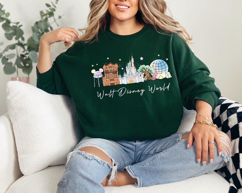May include: A dark green crewneck sweatshirt featuring a graphic print of the Walt Disney World skyline, including the castle, water tower, and park icons, with the text Walt Disney World written in white cursive script below the illustration.