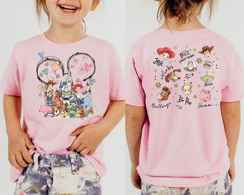 Op de afbeelding: Een lichtroze T-shirt met een Disney-thema. De voorkant toont een Mickey Mouse oor-omtrek met vuurwerk en Disney-personages. De achterkant toont karakterportretten en namen, waaronder Woody en Buzz Lightyear.